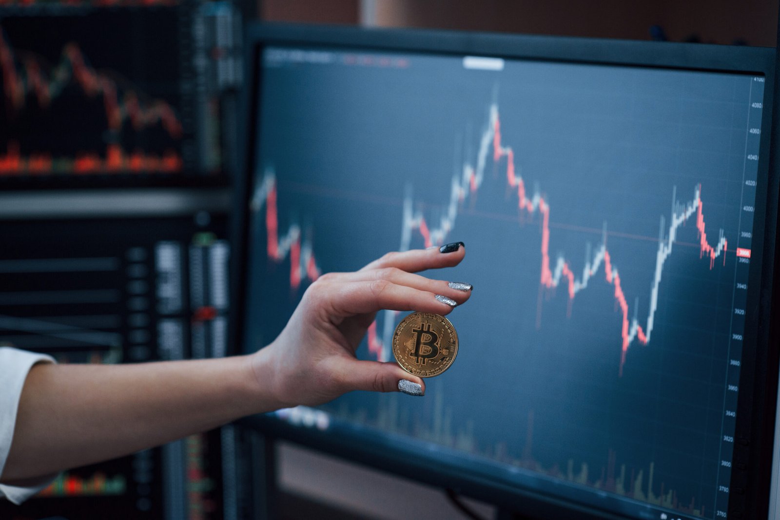 Front view. Woman's hand holding bitcoin in modern office with many monitors with graphs